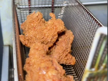 A basket of chicken lifting out of the fryer in the Fri Kitchn kitchen.