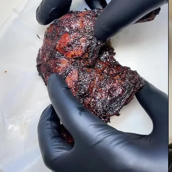 Dark charred jerk style chicken held in gloved hands.